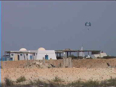 On the path to the sea, some local buildings and a parachutist pulled by a boat