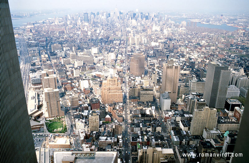 The view north to Manhattan from the covered viewing room on the 107th floor of WTC 2. The dark structure at left is WTC 1. The straight road in the middle of the picture is 5th Avenue. Far on the horizon you can barely see the Empire State 